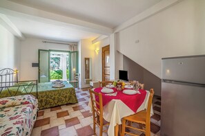Een eethoek met een tafel voor vier personen, een bed met bloemenbedrijf, een koelkast en een trap naar een andere kamer.