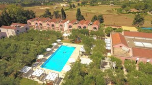 An aerial view of a resort with a swimming pool surrounded by lounge chairs and umbrellas, a large building with arched windows, and a rural landscape in the background. - Borgo Primizia M7 Pool And Sea, Otranto, Italy (Otranto)