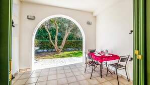 A room with a tiled floor, a table with a red tablecloth, two chairs, and a view through an arched doorway to a garden with trees. - Borgo Primizia M7 Pool And Sea, Otranto, Italy (Otranto)