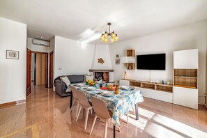 A dining area with a table set for four, a sofa, a fireplace, and a television mounted on the wall.