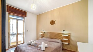A hotel room with a bed, a wooden headboard, a wall-mounted shelf, and a door with a view.