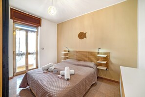 Une chambre d’hôtel avec un lit, une tête de lit en bois, une étagère fixée au mur et une porte donnant sur une vue agréable.