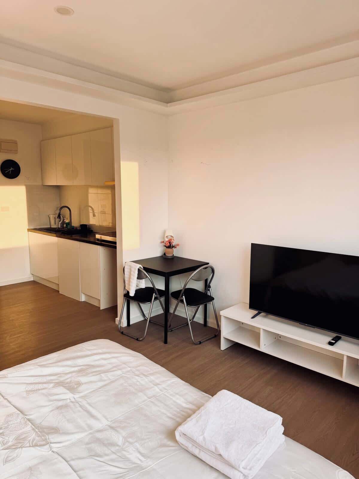 Een compacte hotelkamer met een bed, een televisie, een klein tafeltje met stoelen en een kitchenette op de achtergrond.