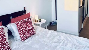 Een slaapkamer met een bed, kussens, een nachtkastje, een lamp en een wanddecoratie.