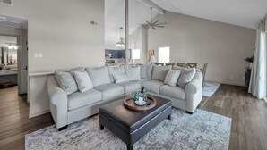 Ein modernes Wohnzimmer mit einem Ecksofa, einem dunklen Couchtisch und einem großen Fenster, das für natürliches Licht sorgt.