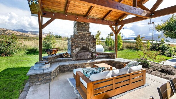 Une terrasse extérieure dotée d’une cheminée en pierre, de sièges en bois et d’une structure en forme de pergola.