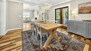 Un espace repas comprenant une table en bois, des chaises blanches, un lustre et un tapis à motifs.