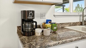 Una cocina con cafetera, una taza y un cesto de cápsulas de café.