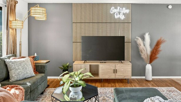 Una sala de estar moderna con una pared gris, un mueble bajo para televisión de madera, un sofá, una mesa de centro con una planta y una lámpara decorativa.