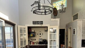 Un comedor moderno con una mesa de vidrio rodeada de sillas, una estación de café y un reloj decorativo.