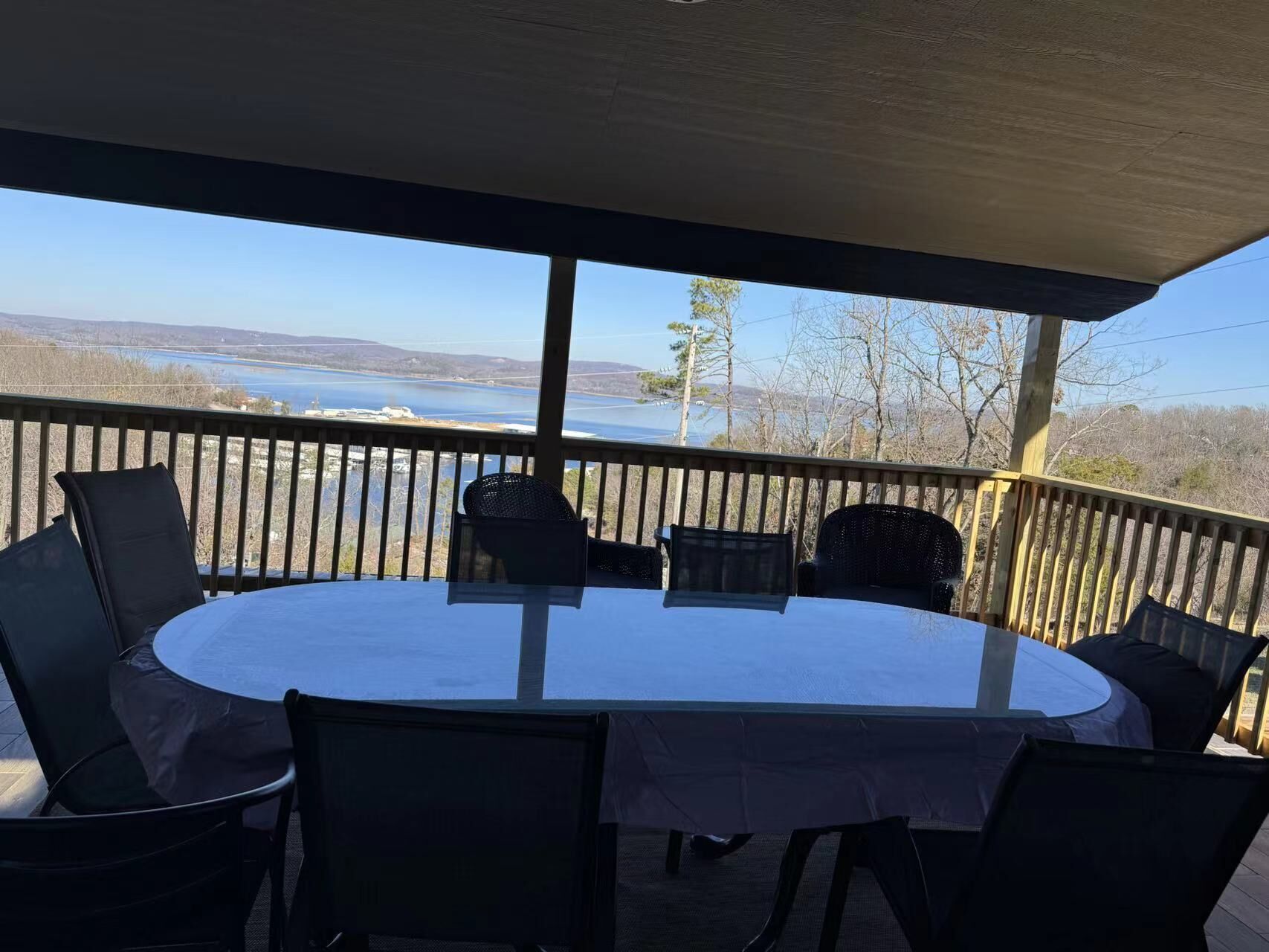 Un espacio de comedor al aire libre cubierto, con una mesa redonda y sillas, con vista a un cuerpo de agua y colinas.