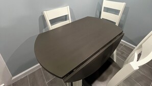 Ett matbord med två vita stolar, en mörk bordsskiva och grå väggar.