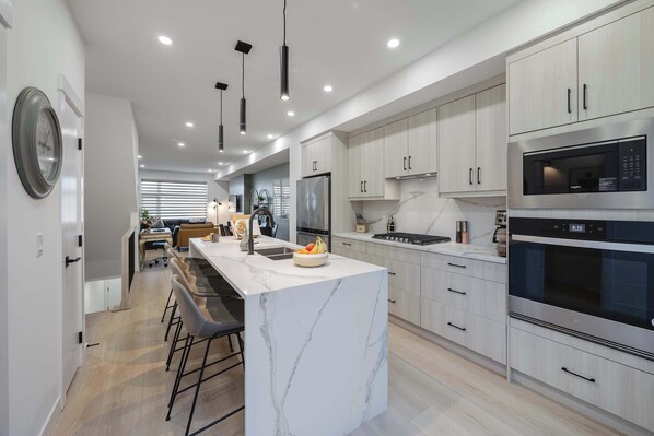 A modern kitchen with a marble island, stainless steel appliances, and a dining area with bar stools.