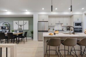 A modern kitchen with stainless steel appliances, a marble island, and a dining area with a table and chairs.