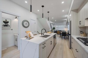 A modern kitchen with a marble island, pendant lighting, and a dining area with a staircase leading to another level.