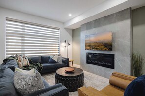 A modern living room with a sofa, a round coffee table, and a flat-screen TV mounted on the wall.