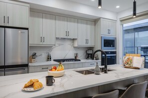 A modern kitchen with a marble countertop, stainless steel appliances, and a large window.