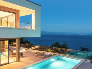 Una casa moderna con piscina, un balcón con telescopio y vistas al mar.