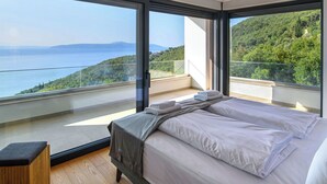 A modern bedroom with a large bed, a wooden nightstand, and a view of a lake and forest. - Marmonte by Interhome (Lovran/Medveja)