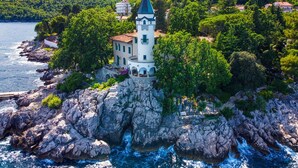 A coastal building with a tower, surrounded by rocky terrain and lush greenery. - Marmonte by Interhome (Lovran/Medveja)