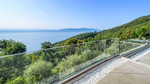 A balcony with a glass railing overlooking a coastal landscape with trees and a view of the sea. - Marmonte by Interhome (Lovran/Medveja)