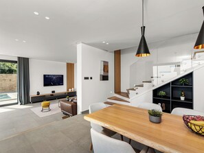 A modern living room with a wooden dining table, white chairs, a TV, and a staircase leading to a loft. - Marmonte by Interhome (Lovran/Medveja)