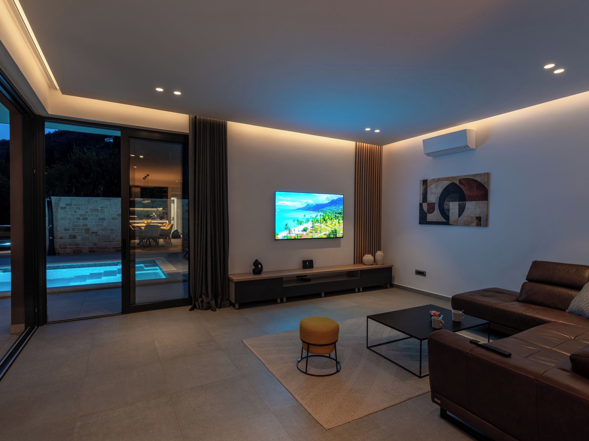 Una sala de estar moderna con un televisor de pantalla plana, un sofá, una mesa de centro y un pequeño otoman.
