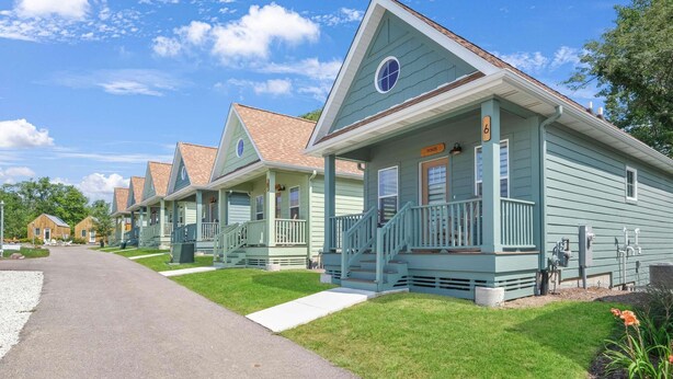 A row of light blue cottages with a central staircase, a clear sky, and a gravel driveway. - Stay in all five Canopies (Ottawa)