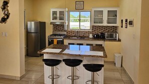 Cocina con una isla central, taburetes de bar, refrigerador, estufa, microondas y una ventana con vistas.