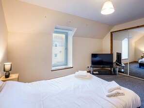 Et hotelværelse med en stor seng, et fladskærms-tv, et skrivebord med en computer og et stort spejl.