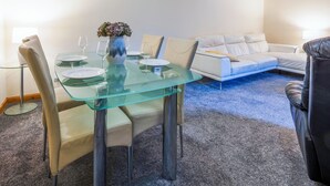 Un salon moderne avec une table à manger en verre, des canapés beige et une petite table d’appoint sur laquelle est posé un vase.