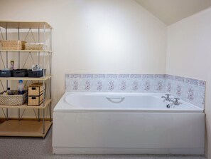 Et badeværelse med et hvidt badekar, en hylde med kurve og et flisebeklædt bagpanel.