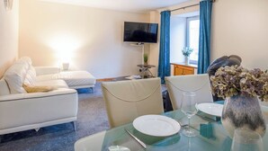 Une chambre d’hôtel moderne, équipée d’un canapé, d’une table à manger dressée avec des assiettes et des verres, d’une télévision et d’une fenêtre avec des rideaux.