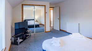 Une chambre d’hôtel moderne dotée d’une télévision à écran plat, d’un lit avec du linge de maison blanc, d’une porte en verre donnant sur la salle de bain et d’un radiateur.