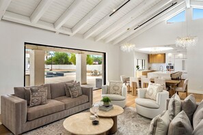 A spacious living area with a sofa, armchairs, and a coffee table. A kitchen with modern appliances and a dining area with chairs is visible in the background. - The Tiercel – 20-Person Spa, Heated Salt Pool, Pickleball, 2025 Renovation (Scottsdale)