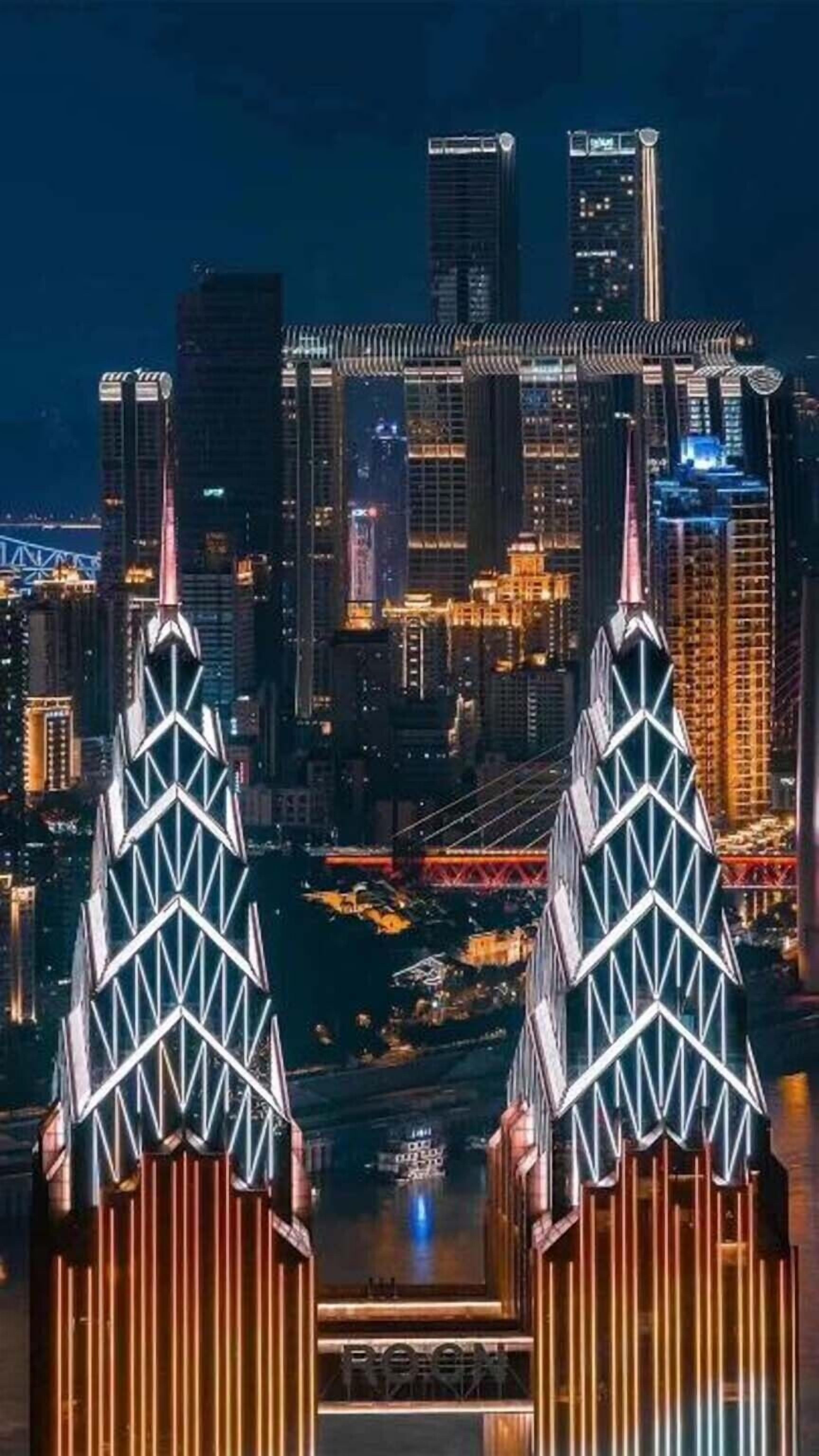 Un paisaje urbano nocturno con dos rascacielos destacados que presentan un diseño geométrico distintivo.