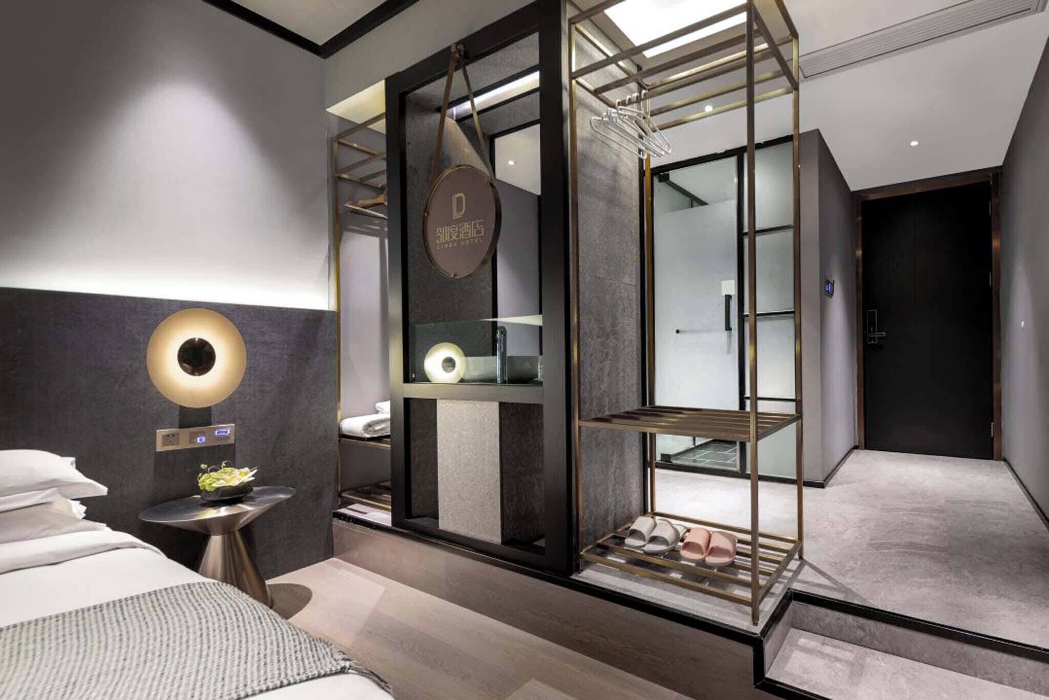 Une chambre d’hôtel moderne comprenant un lit, une table de chevet avec une lampe, une armoire et un porte-chaussures.