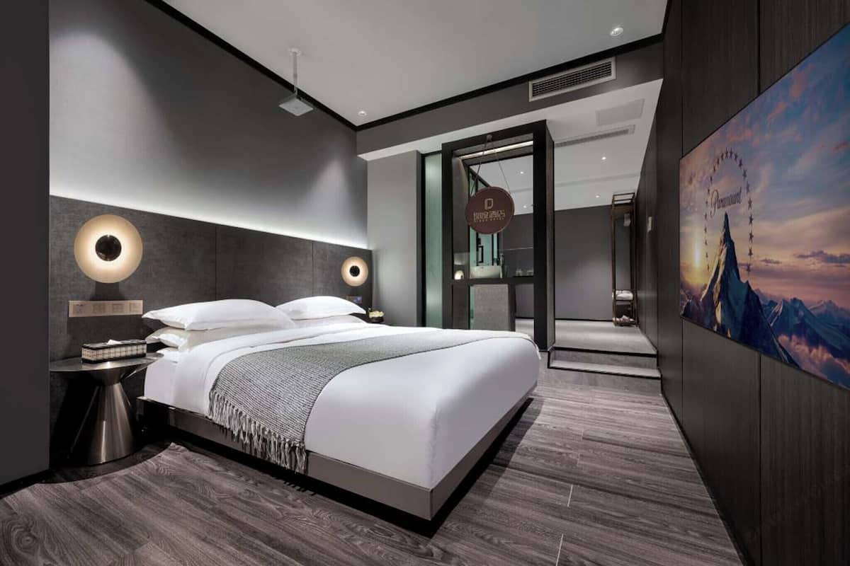 Une chambre d’hôtel moderne, dotée d’un grand lit, de lampes de chevet et offrant une vue sur le paysage urbain par la fenêtre.