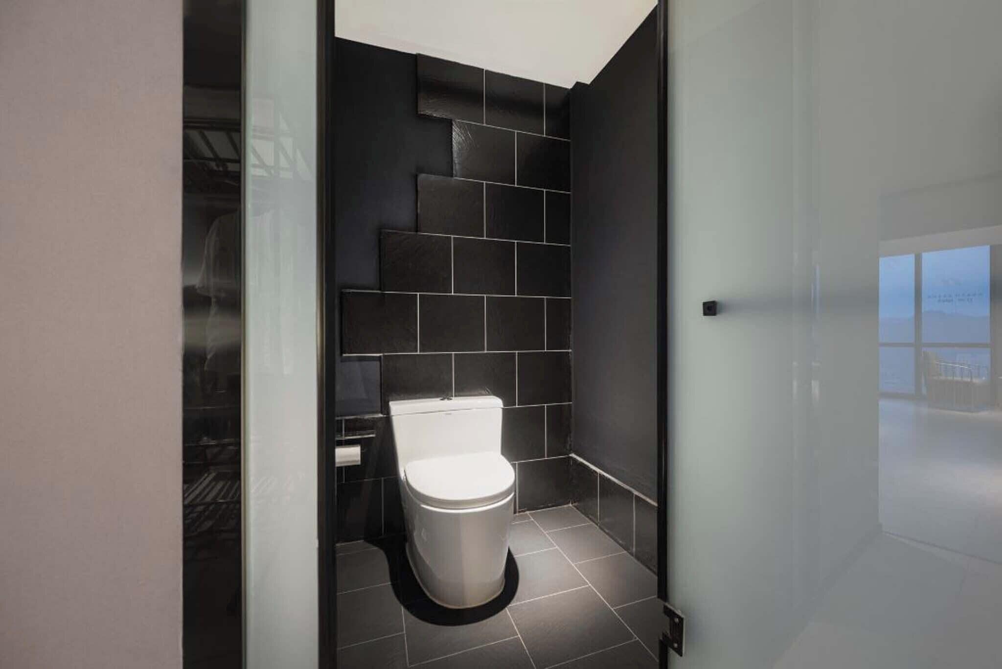 A modern bathroom with a white toilet, dark tiled walls, and a glass shower enclosure.
