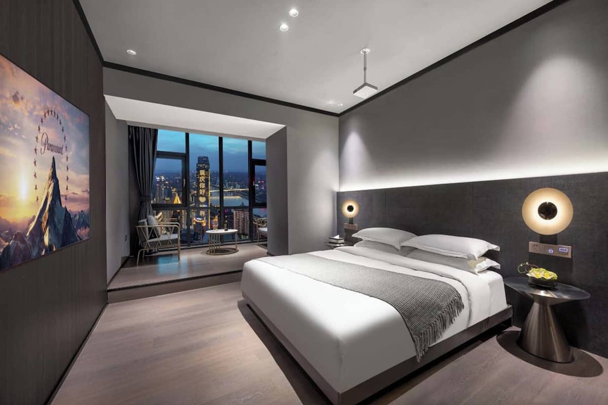 Une chambre d’hôtel moderne dotée d’un grand lit, offrant une vue sur la ville, et présentant un design minimaliste.