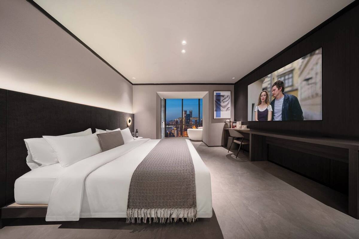 Une chambre d’hôtel moderne, dotée d’un grand lit, d’un bureau et offrant une vue sur la ville par la fenêtre.