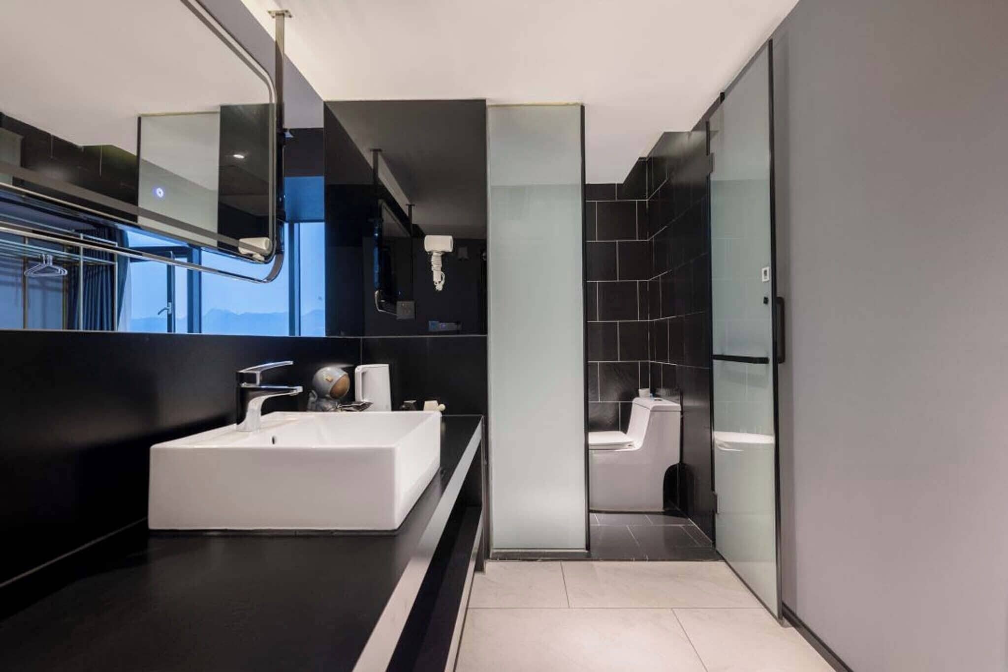 Une salle de bain moderne avec un grand lavabo blanc, une douche en verre et un mur recouvert de carreaux foncés.