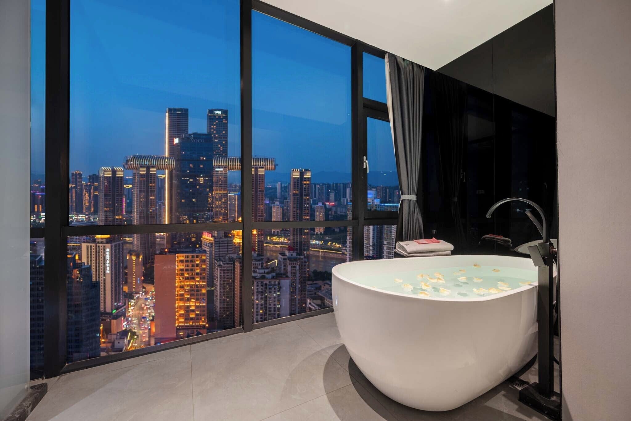 Une salle de bain moderne avec une grande baignoire, un meuble-lavabo et une vue sur le paysage urbain au crépuscule.