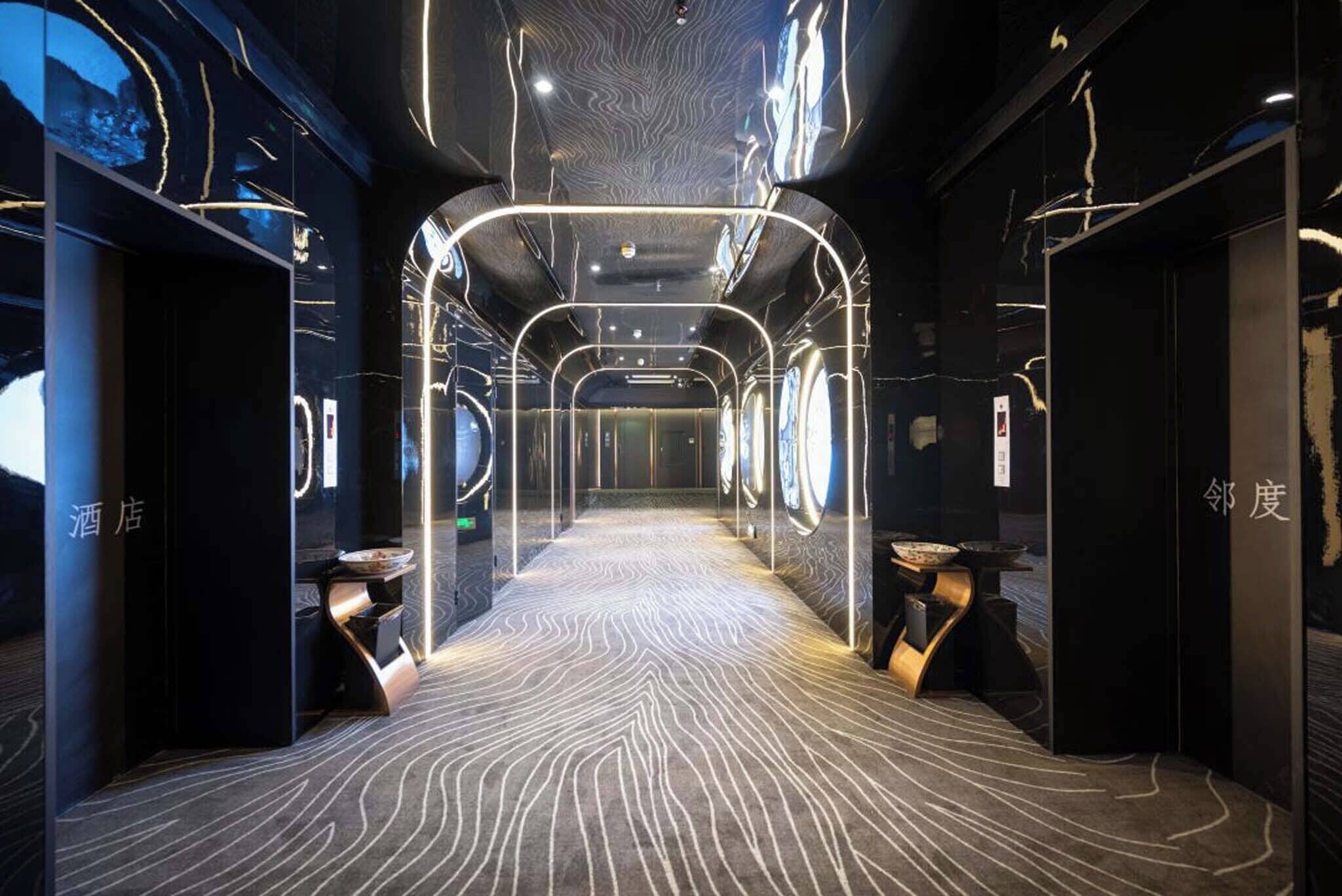 A modern hotel corridor with a patterned floor, glass partitions, and minimalist decor.