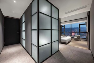 Een moderne hotelkamer met een groot bed, een zithoek en een stadsgezicht door grote ramen.