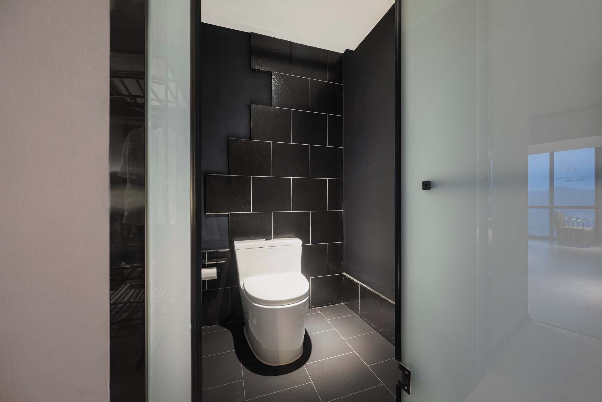 A modern bathroom with a white toilet, dark tiled walls, and a glass shower enclosure.