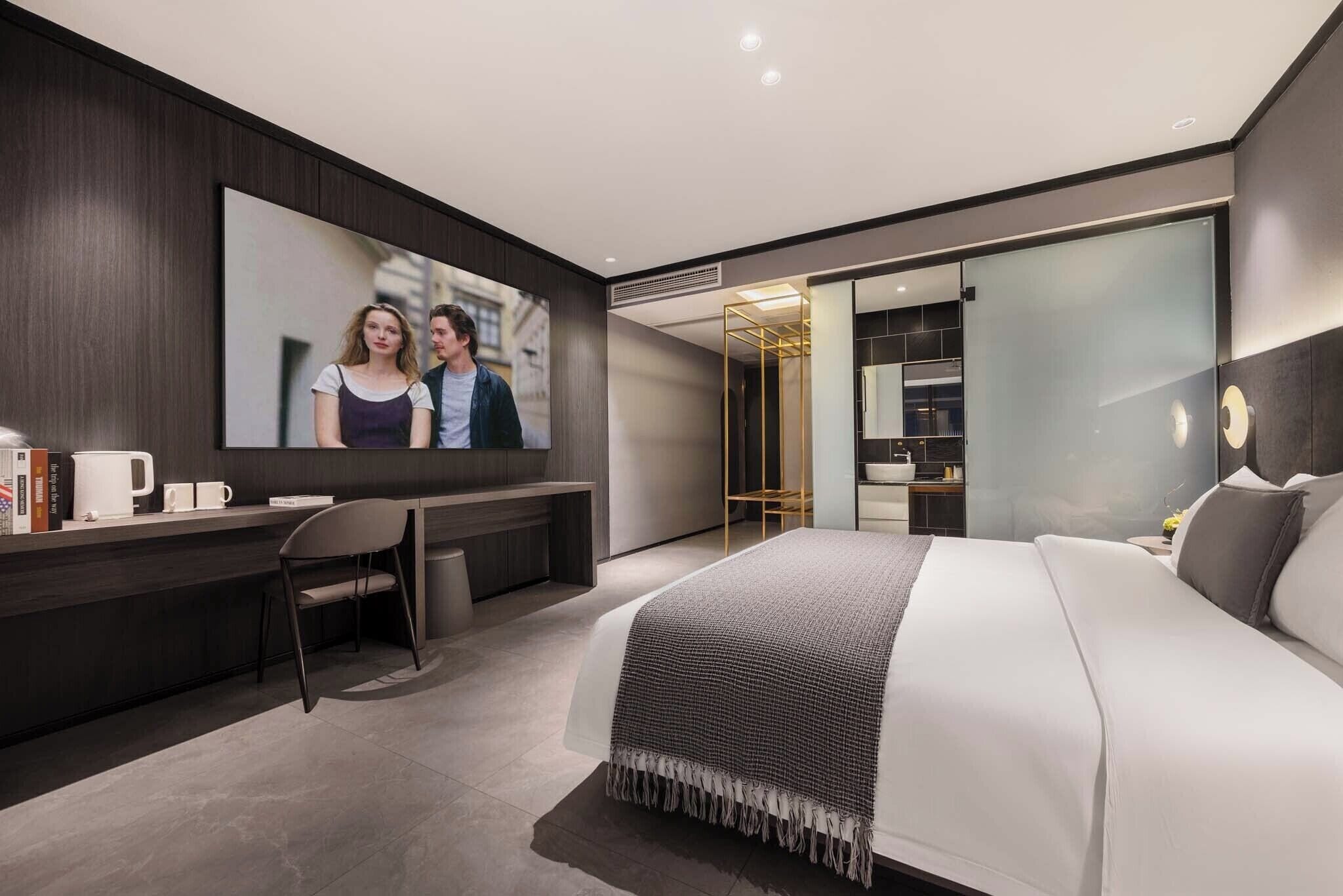 Una habitación de hotel moderna con una cama grande, un escritorio con silla, un espejo amplio y un armario.