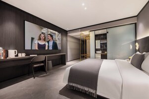 Una habitación de hotel moderna con una cama grande, un escritorio con silla, un espejo amplio y un armario.