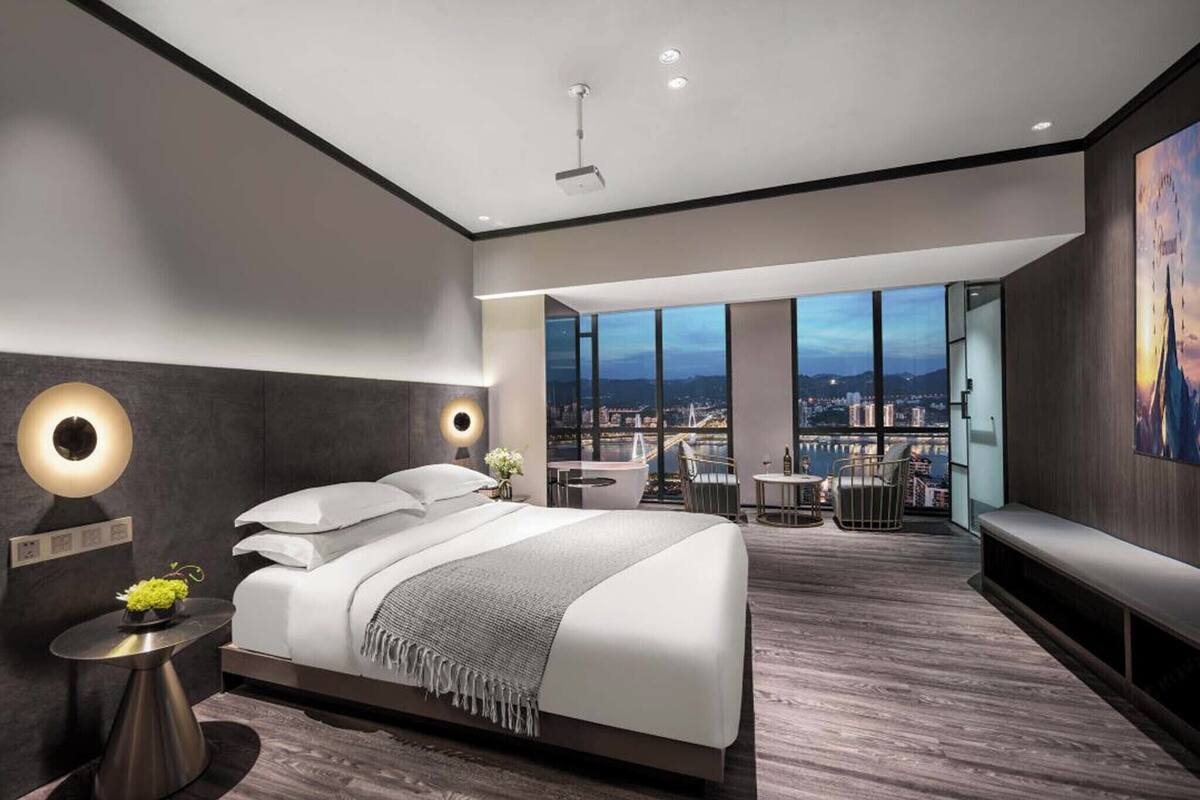 Une chambre moderne avec un grand lit, un balcon offrant une vue sur la ville et une table ronde avec des chaises.