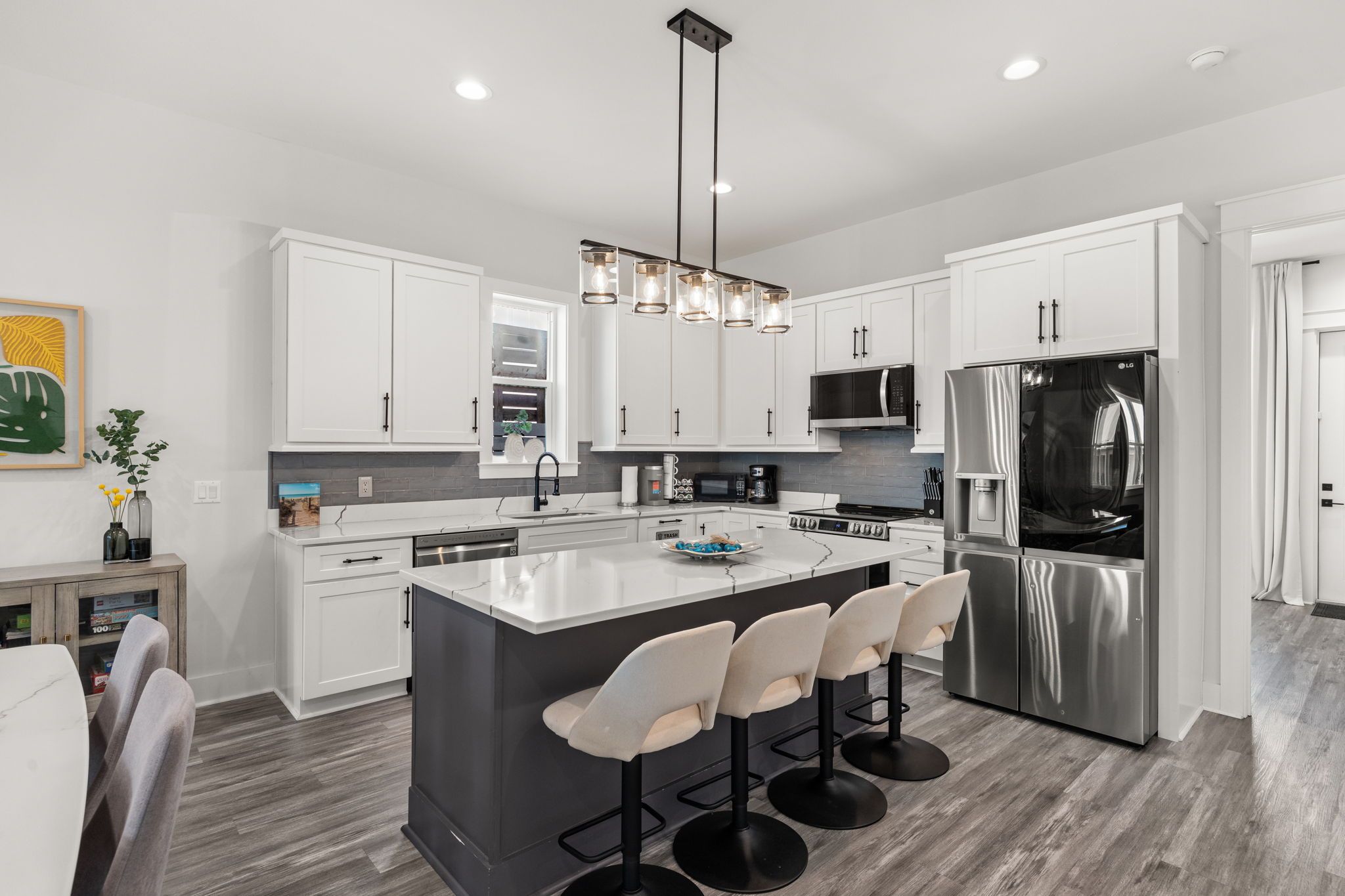 A modern kitchen with white cabinets, a central island with bar stools, stainless steel appliances, and pendant lighting.